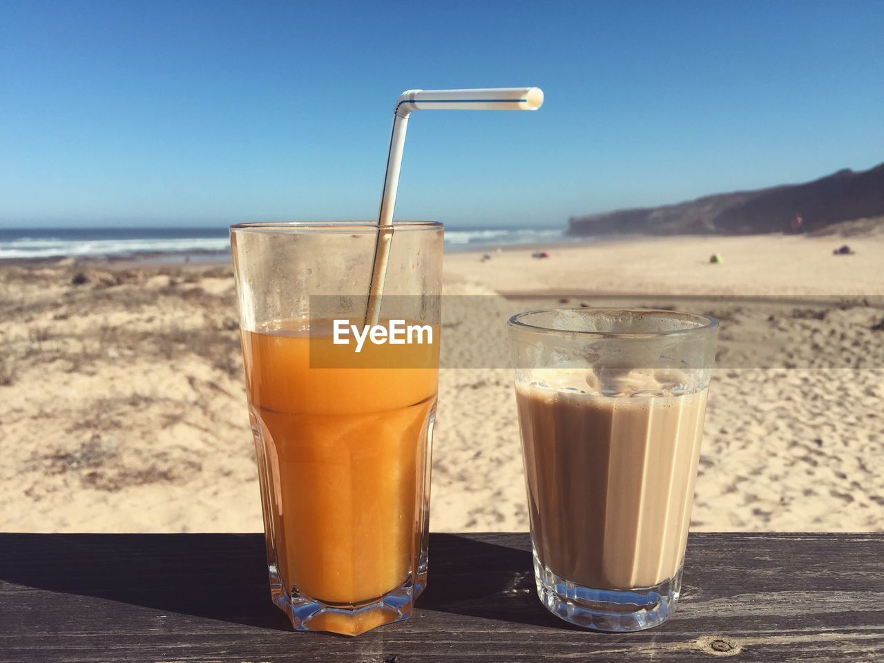 Close-up of orange juice by coffee on table at sandy beach
