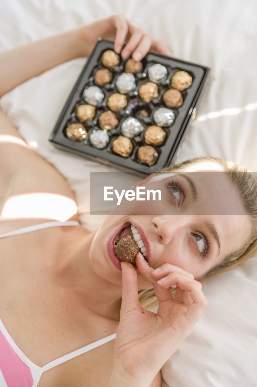 High angle view of thoughtful woman eating chocolate while lying on bed
