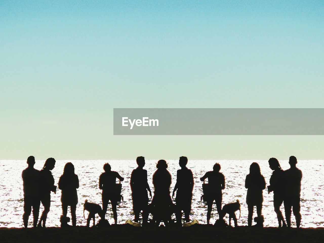 Silhouette people standing at beach against clear sky