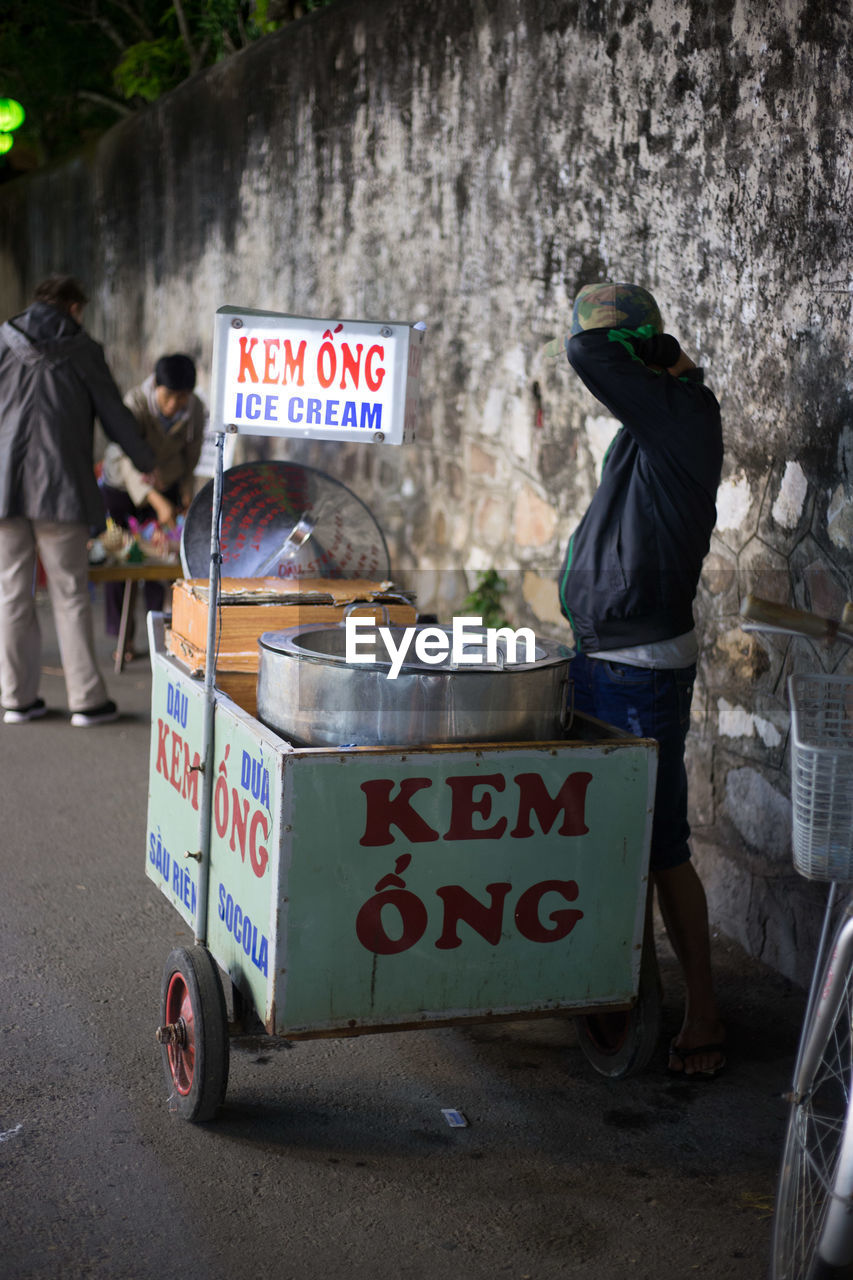 Vendor standing with ice cream stand by wall