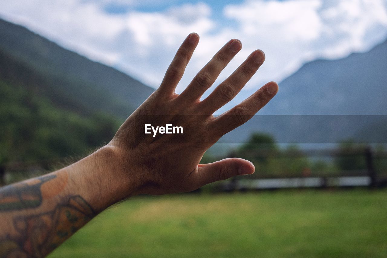 Cropped hand of man gesturing stop sign against mountains