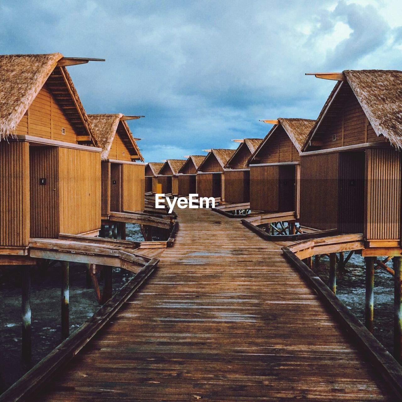 Stilt houses in row over river against cloudy sky