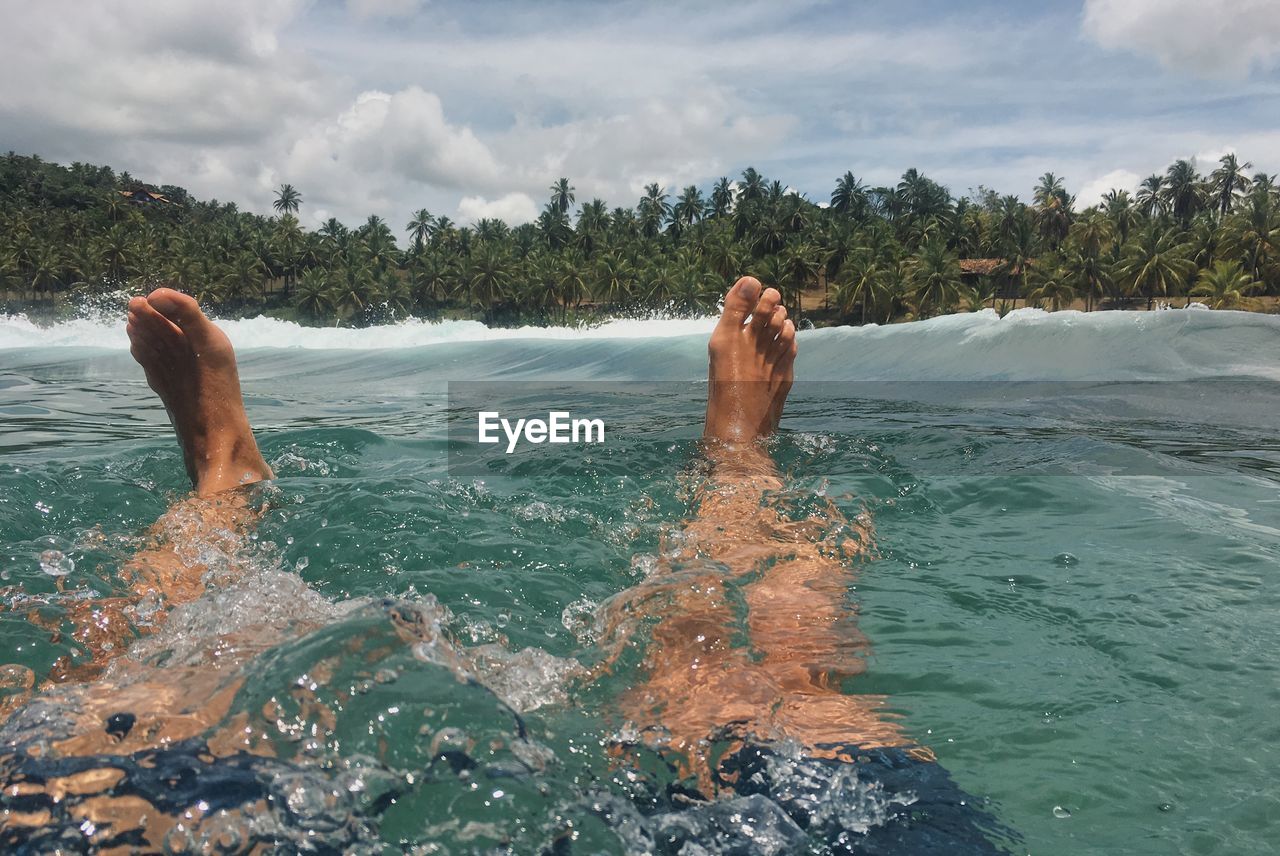 Low section of man swimming in sea against sky