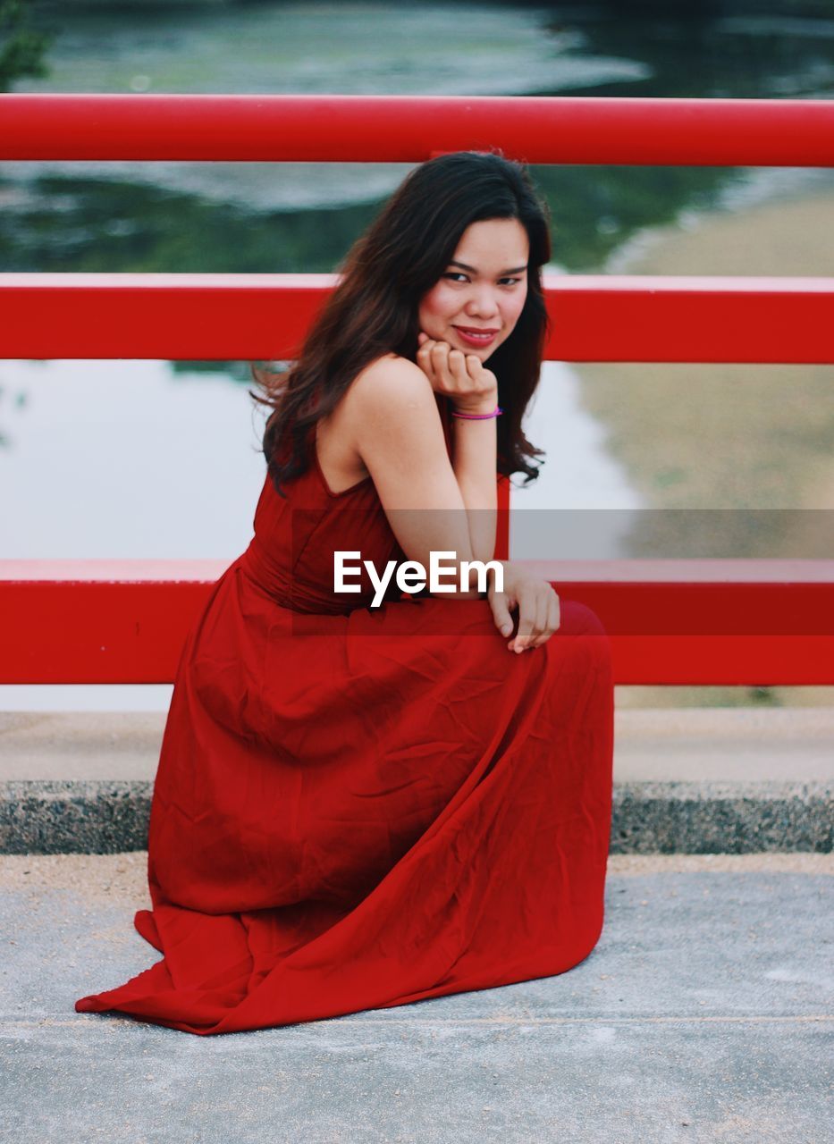 Portrait of beautiful young woman sitting by railing