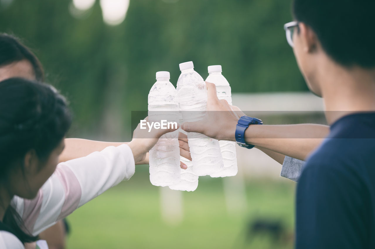 Cropped image of friends toasting water bottles while standing in park