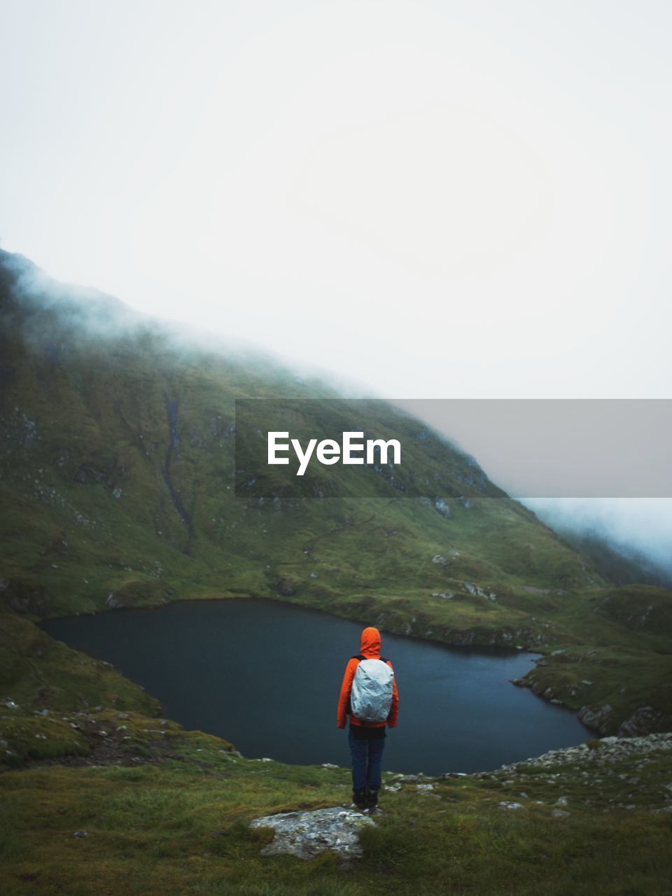 REAR VIEW OF BOY STANDING ON MOUNTAIN AGAINST SKY