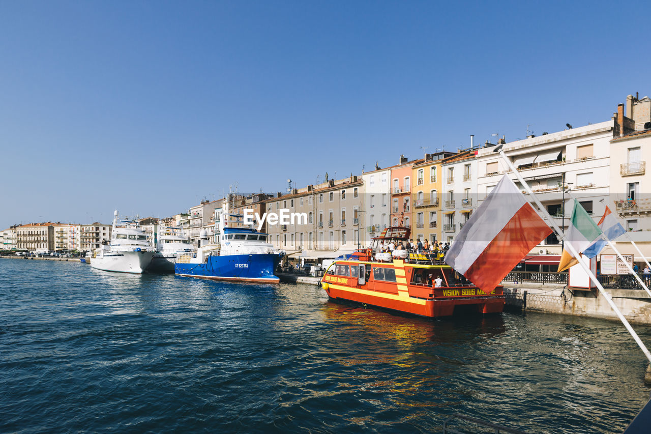 Boats in canal by buildings against clear blue sky