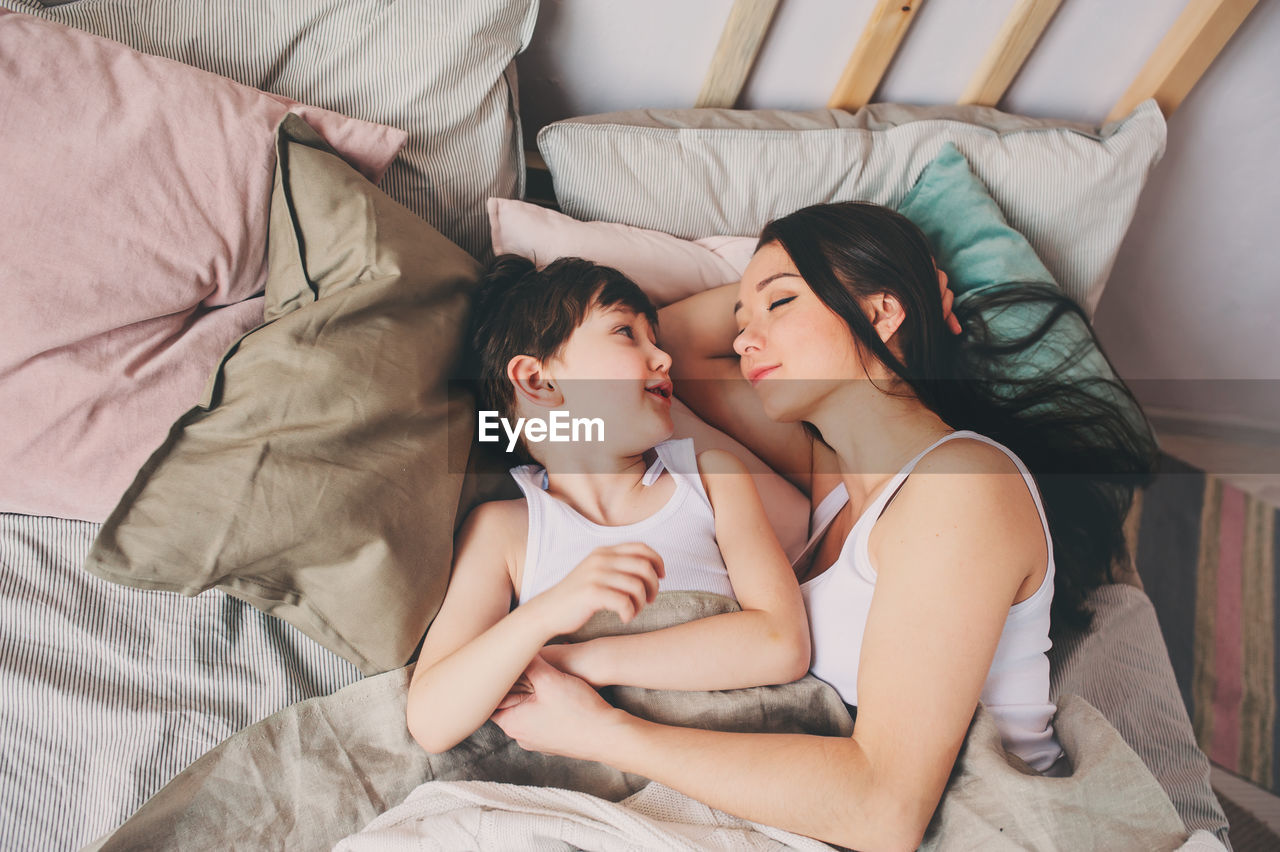 High angle view of smiling mother sleeping with cute son on bed at home