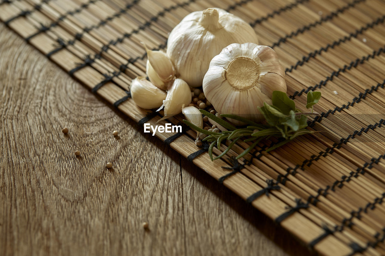 High angle view of garlic and peppercorns with herbs on wooden table