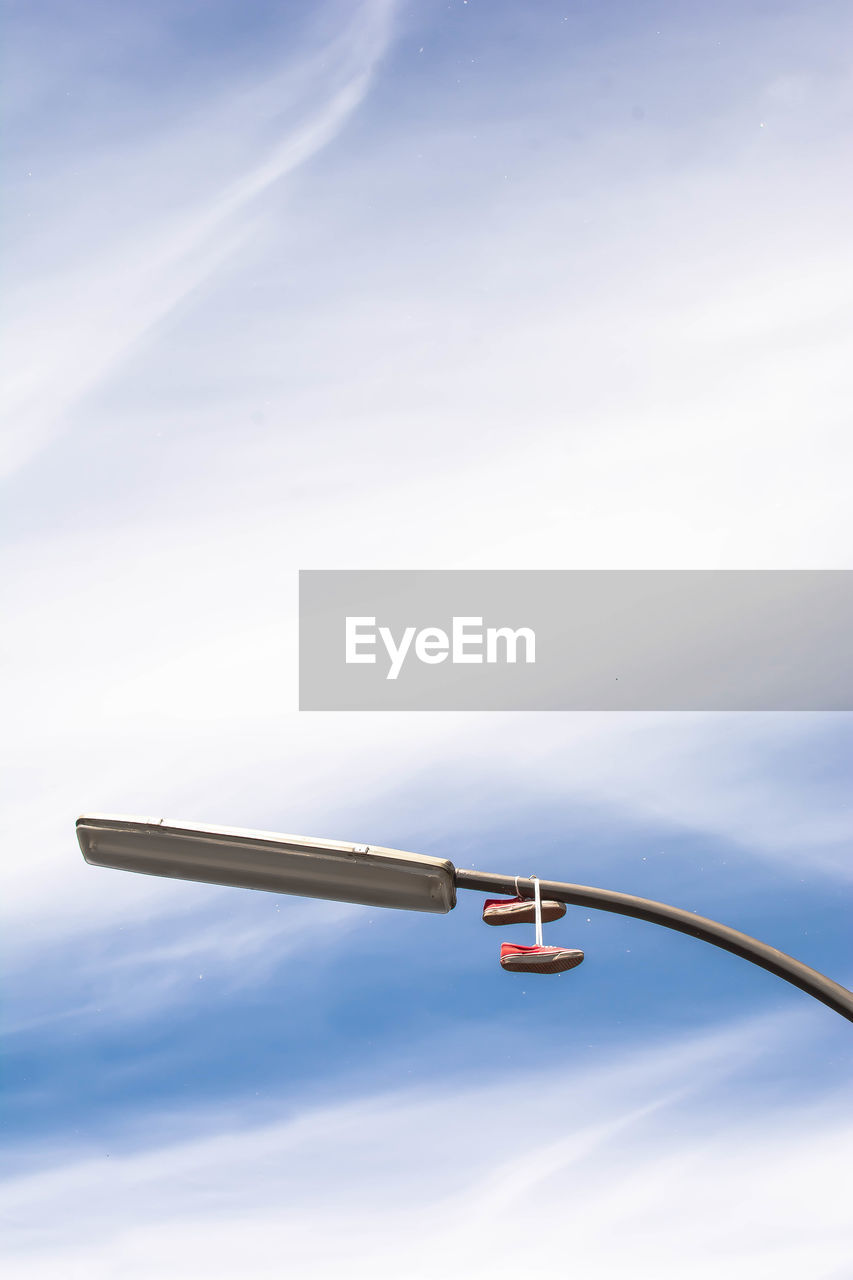 Low angle view of shoes hanging on street light against cloudy sky