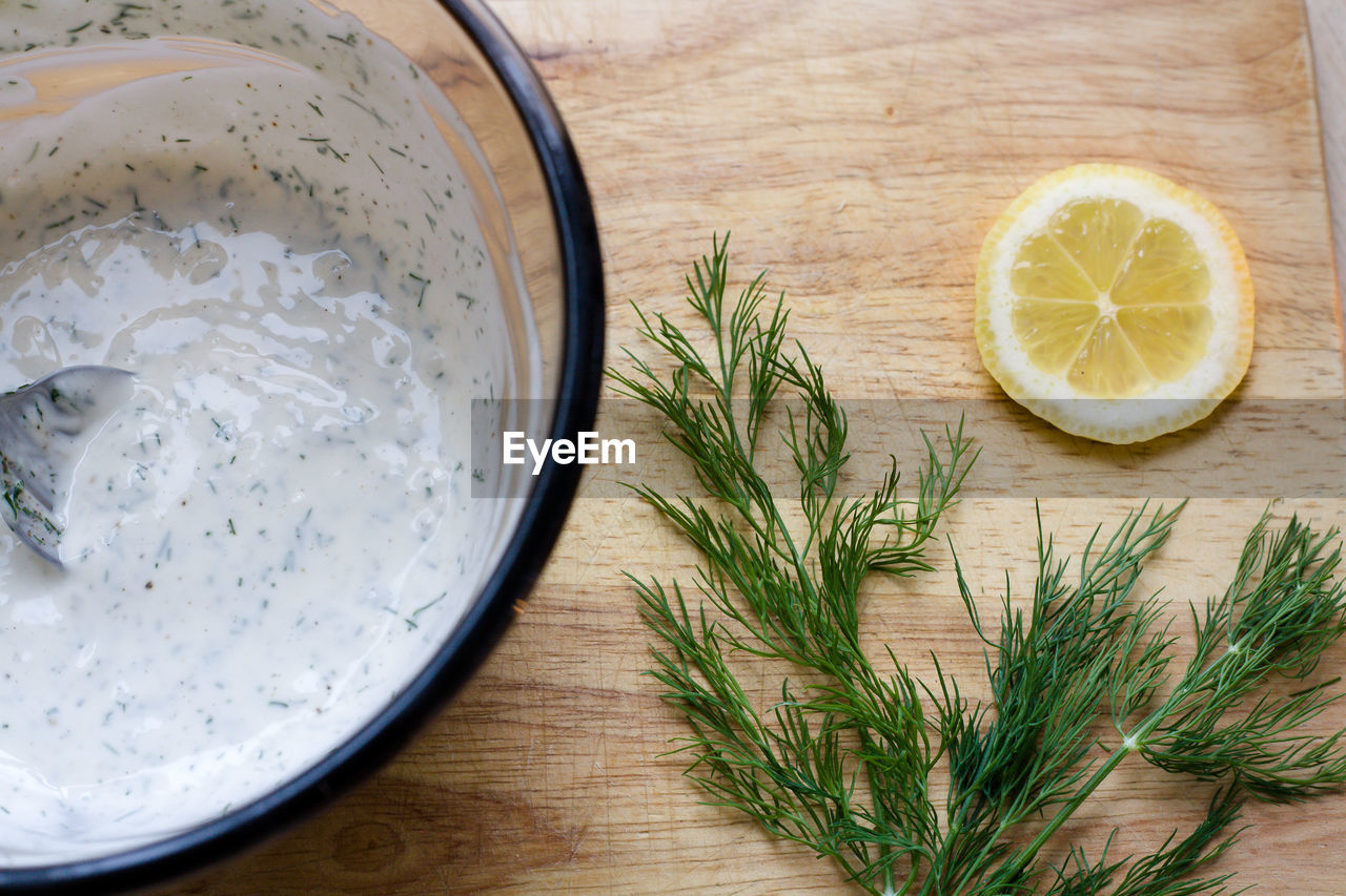 High angle view of mayonnaise in bowl by lemon slice and rosemary on cutting board