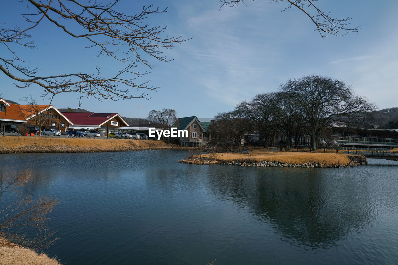 Scenic view of river by houses and trees against sky