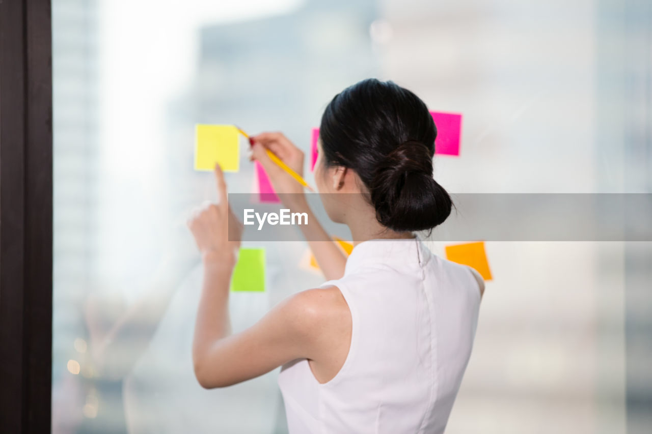 Rear view of a woman writing on sticky paper 