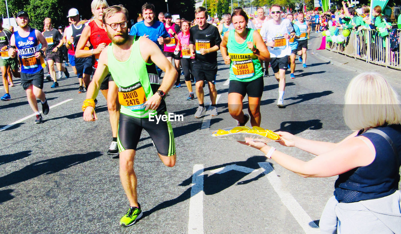 REAR VIEW OF PEOPLE RUNNING ON ROAD