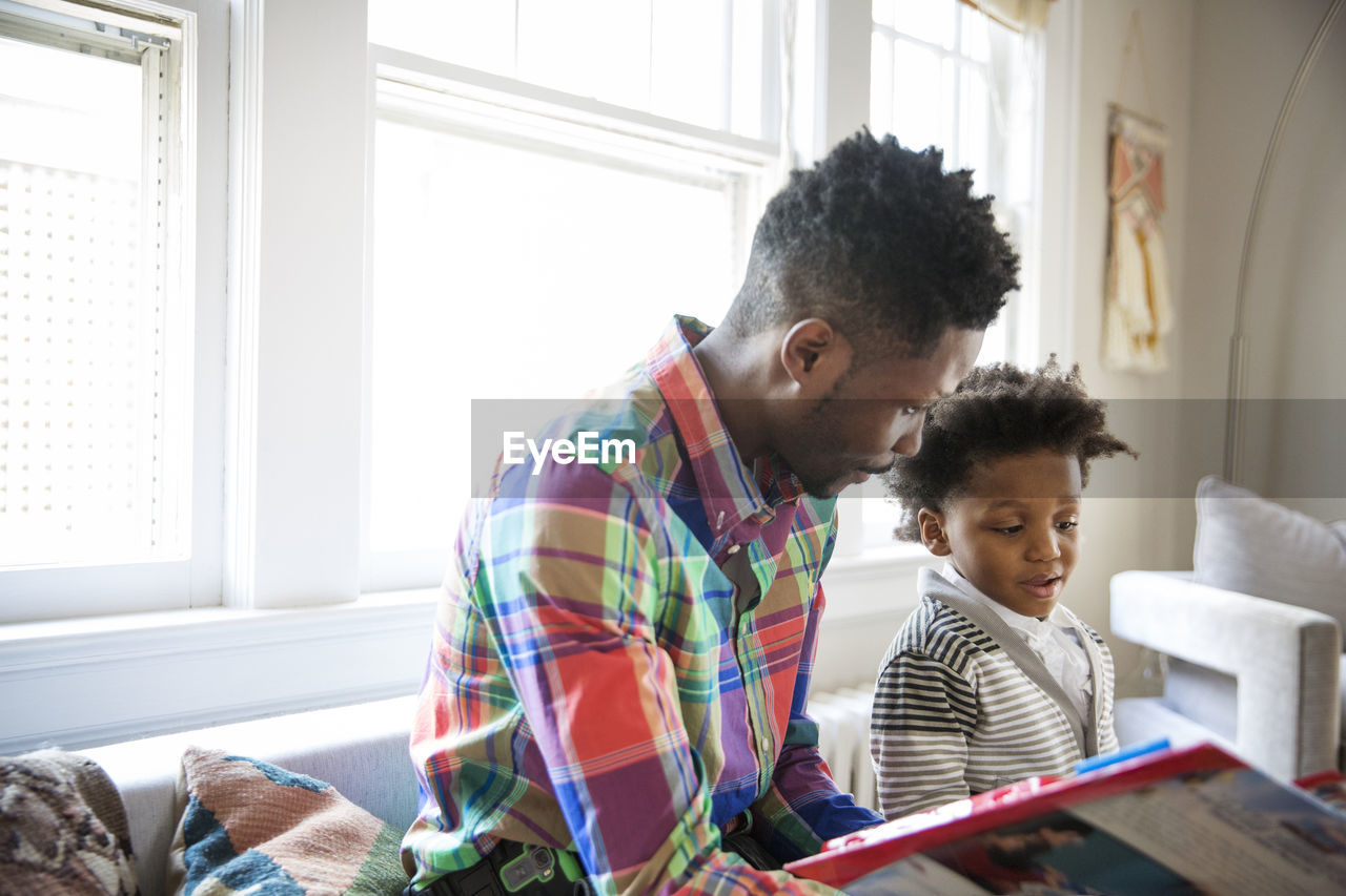 Father and young son reading book together at home