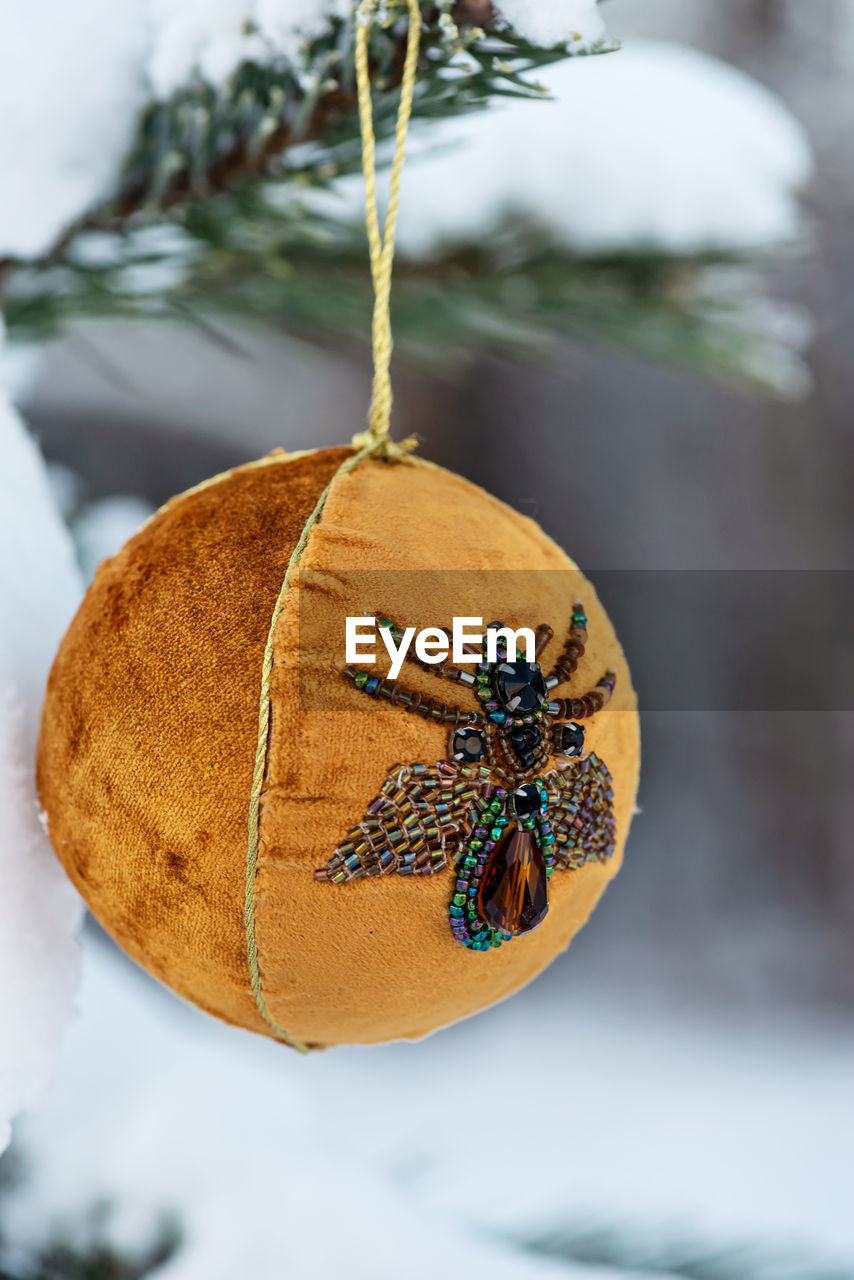 Hanging orange christmas ball on spruce and over blurred background