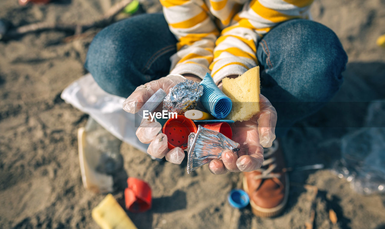 Close-up high angle view of boy holding garbage while crouching at beach