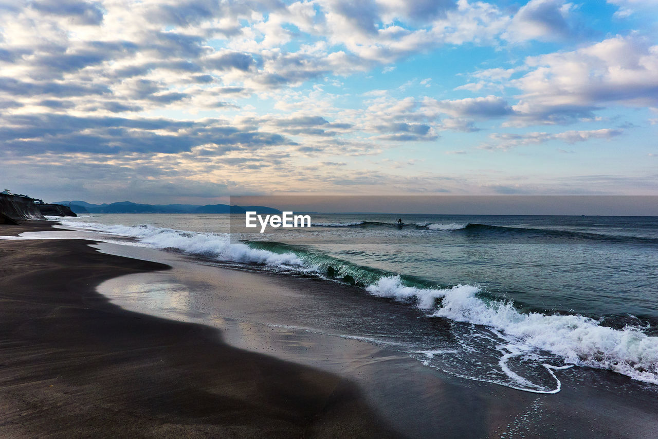 Scenic view of sea with crashing waves against dramatic sky during sunrise