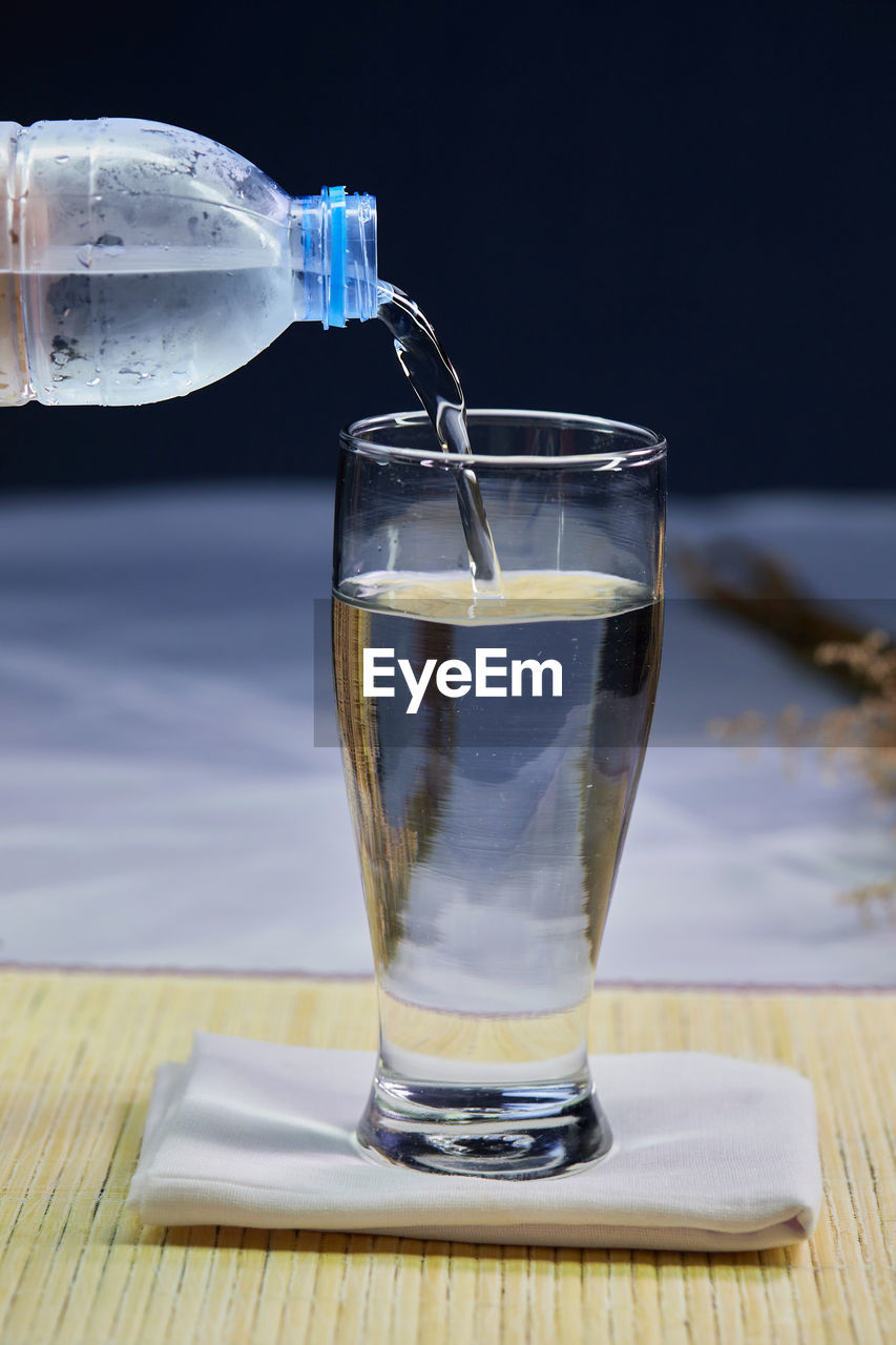 Hand holding bottle pouring water into a drinking glass