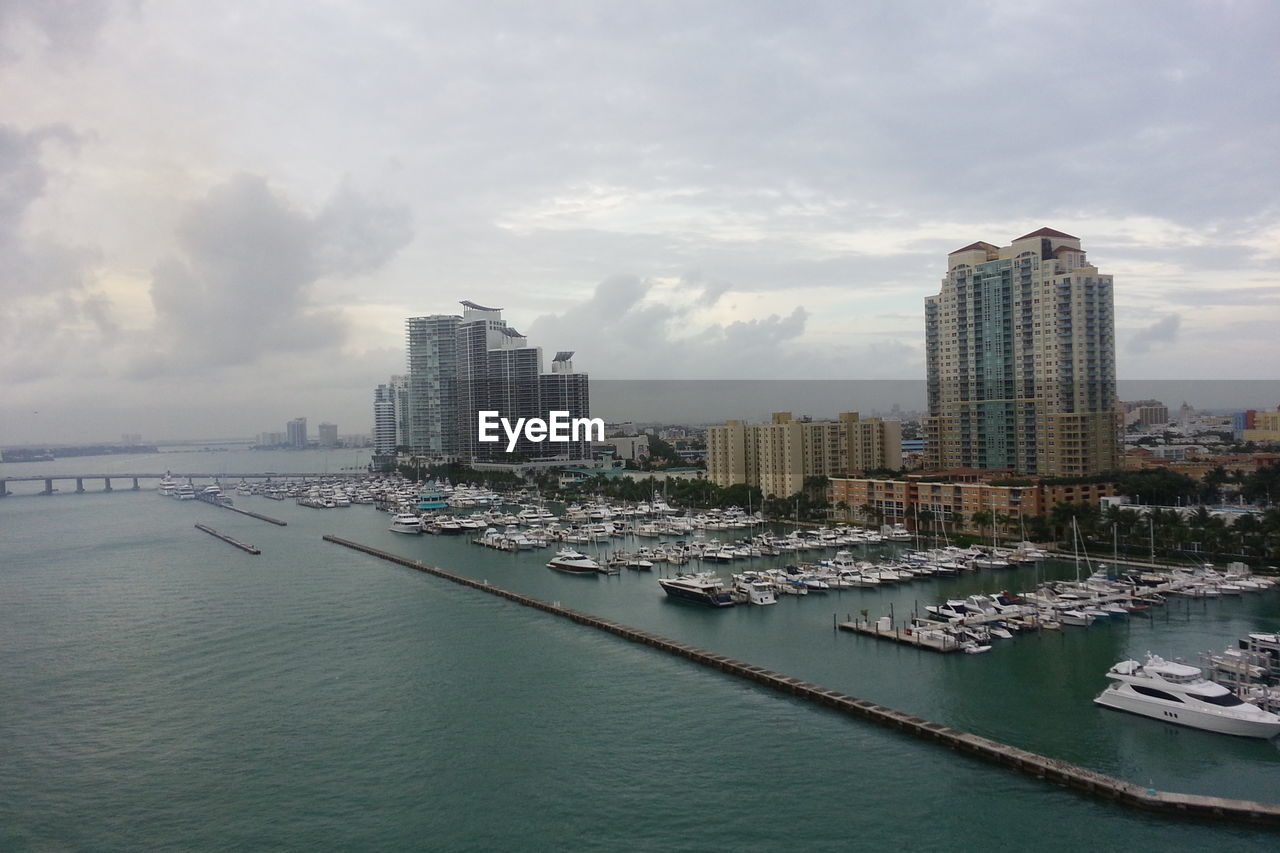 Sailboats moored at harbor by city against sky