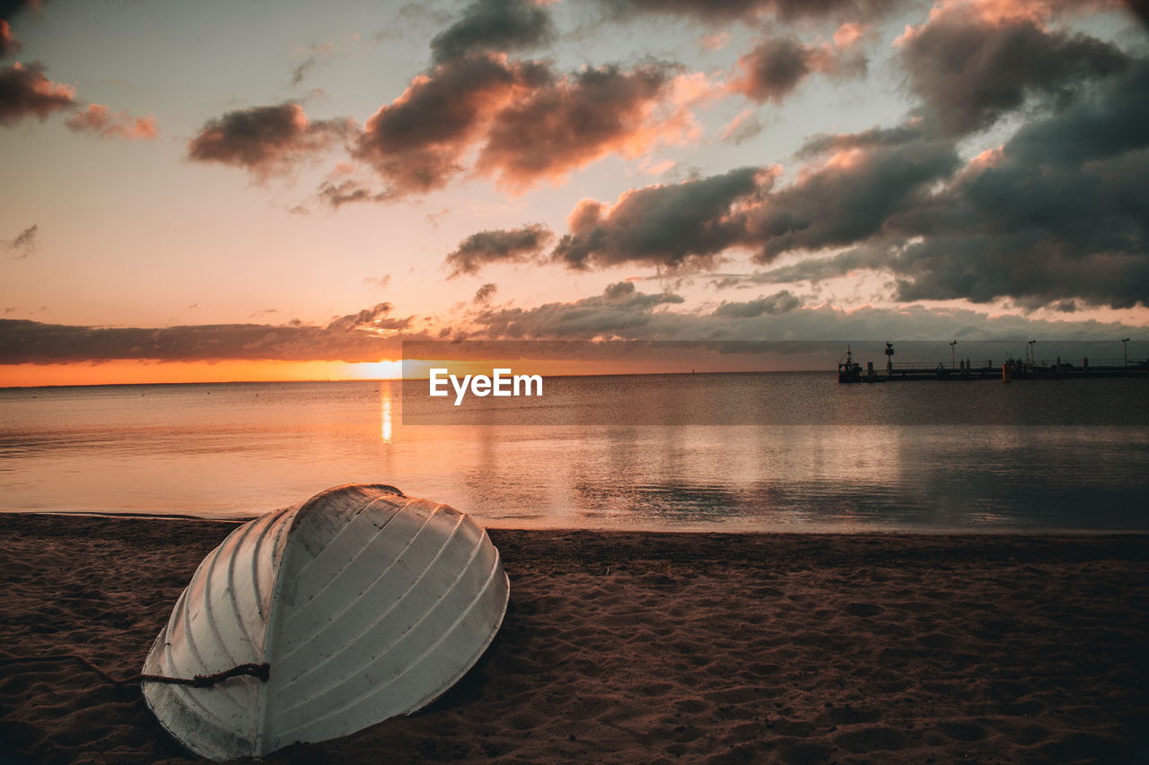 Upside down boat moored on shore at beach against sky during sunset