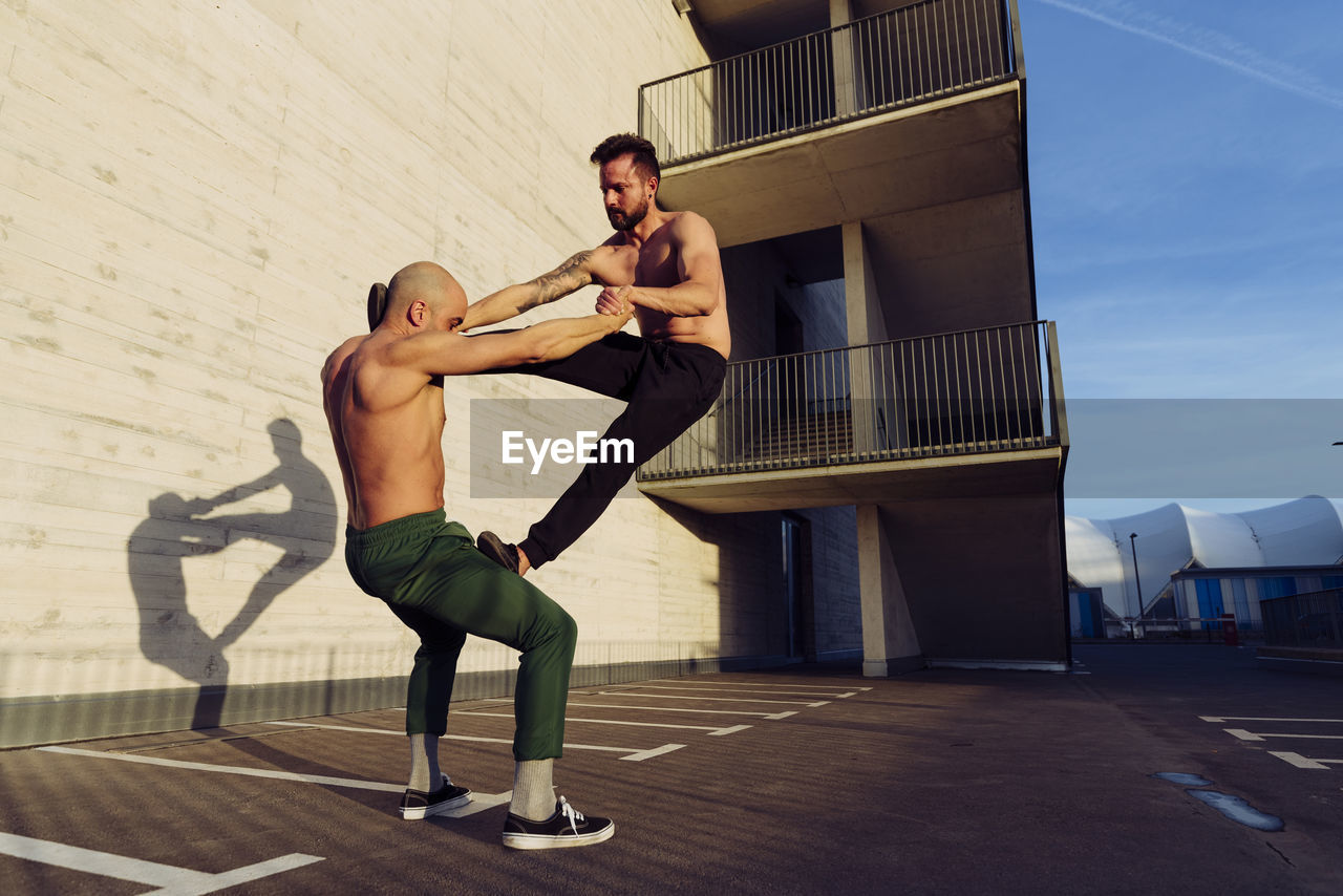 Young athletic shirtless men doing an urban workout outdoors practicing balance exercises