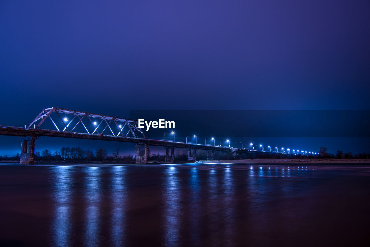 Low angle view of illuminated bridge over frozen river at night