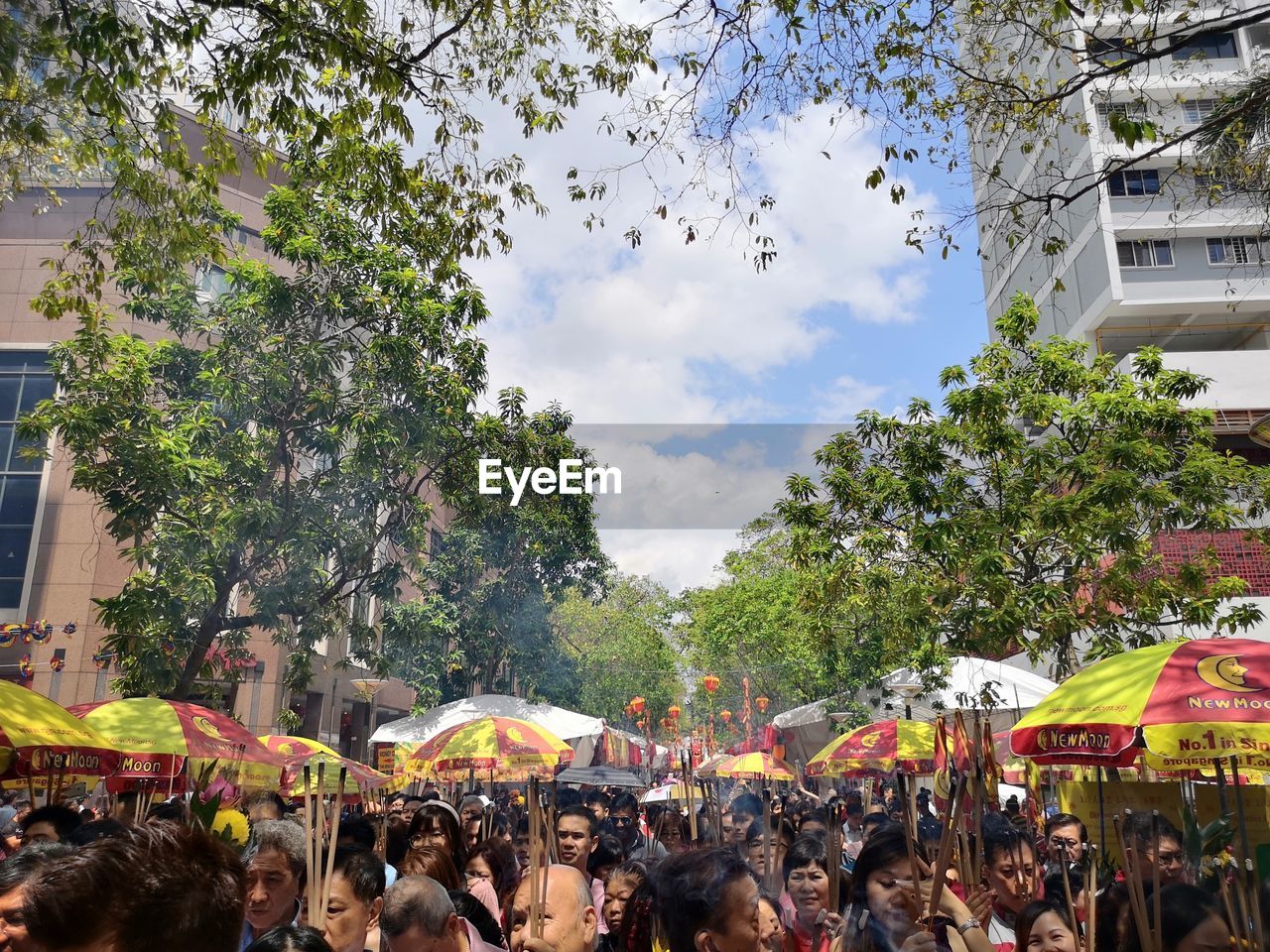 PEOPLE ON STREET AMIDST TREES AGAINST SKY