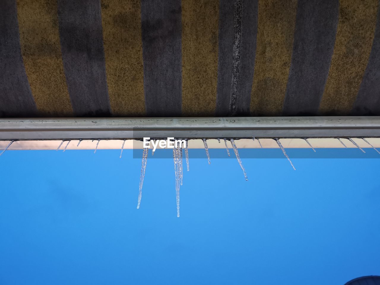 Low angle view of icicles hanging against clear blue sky