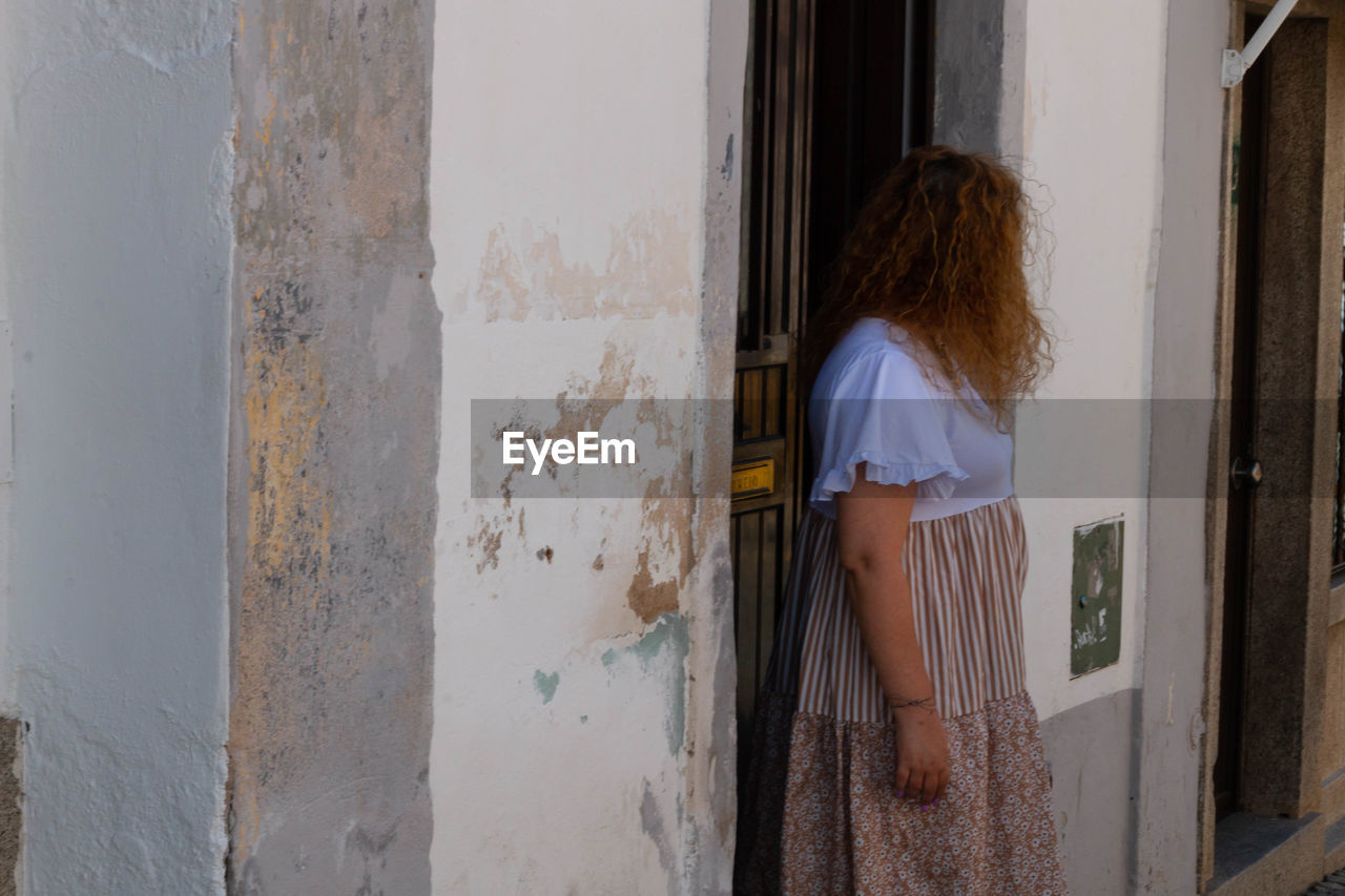 REAR VIEW OF WOMAN STANDING AT ENTRANCE OF BUILDING