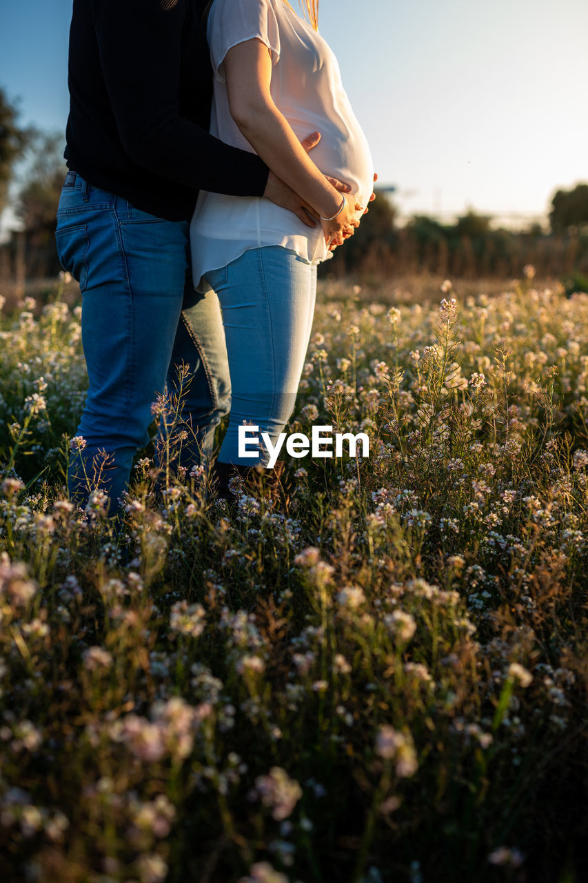 LOW SECTION OF PEOPLE STANDING ON FIELD BY PLANTS