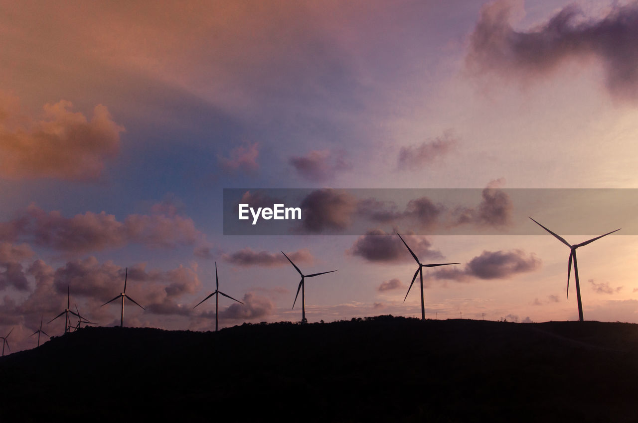 SILHOUETTE WINDMILLS ON FIELD AGAINST SKY DURING SUNSET