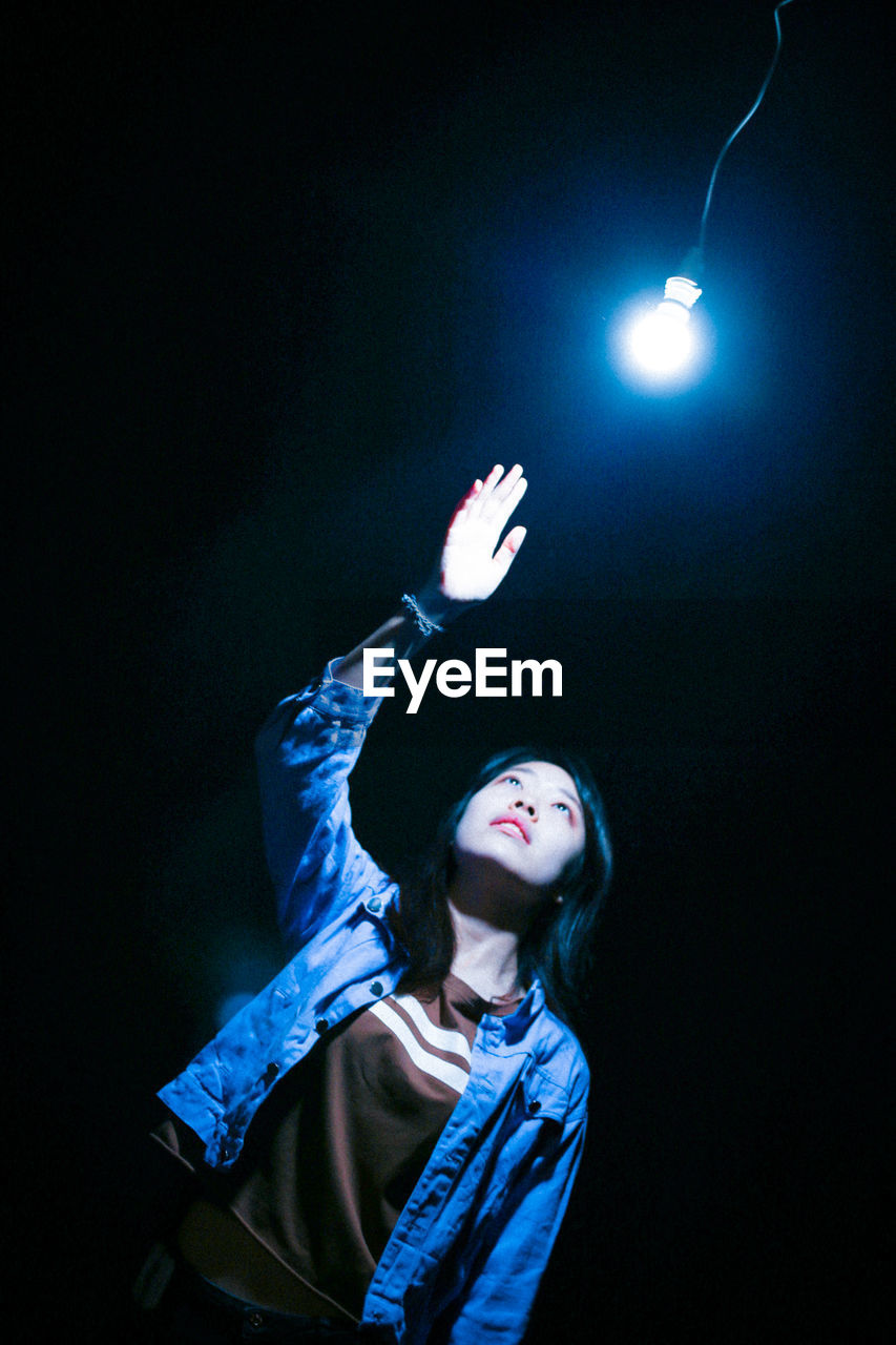 YOUNG WOMAN LOOKING AT ILLUMINATED LAMP