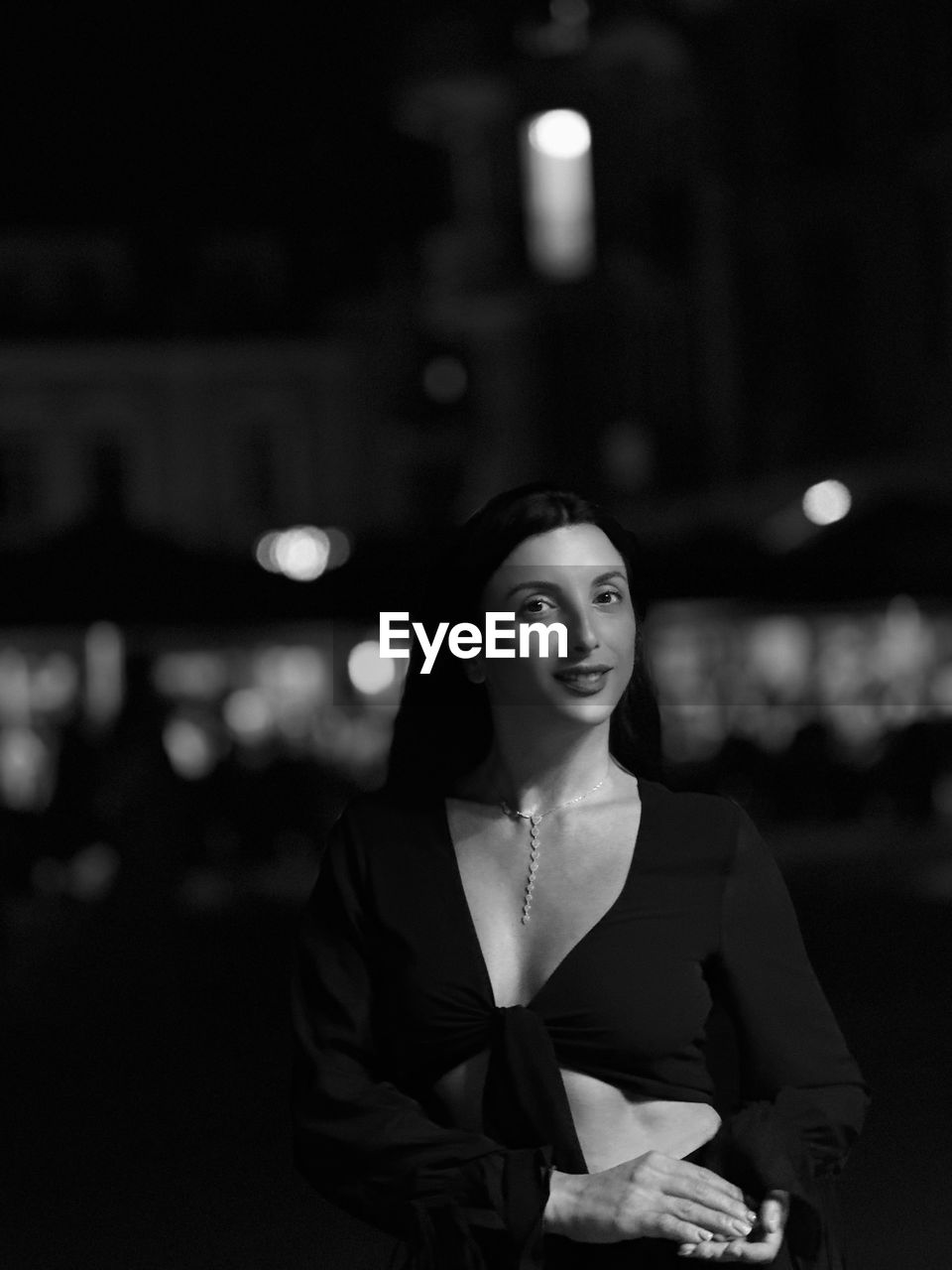 portrait of young woman standing against illuminated city at night