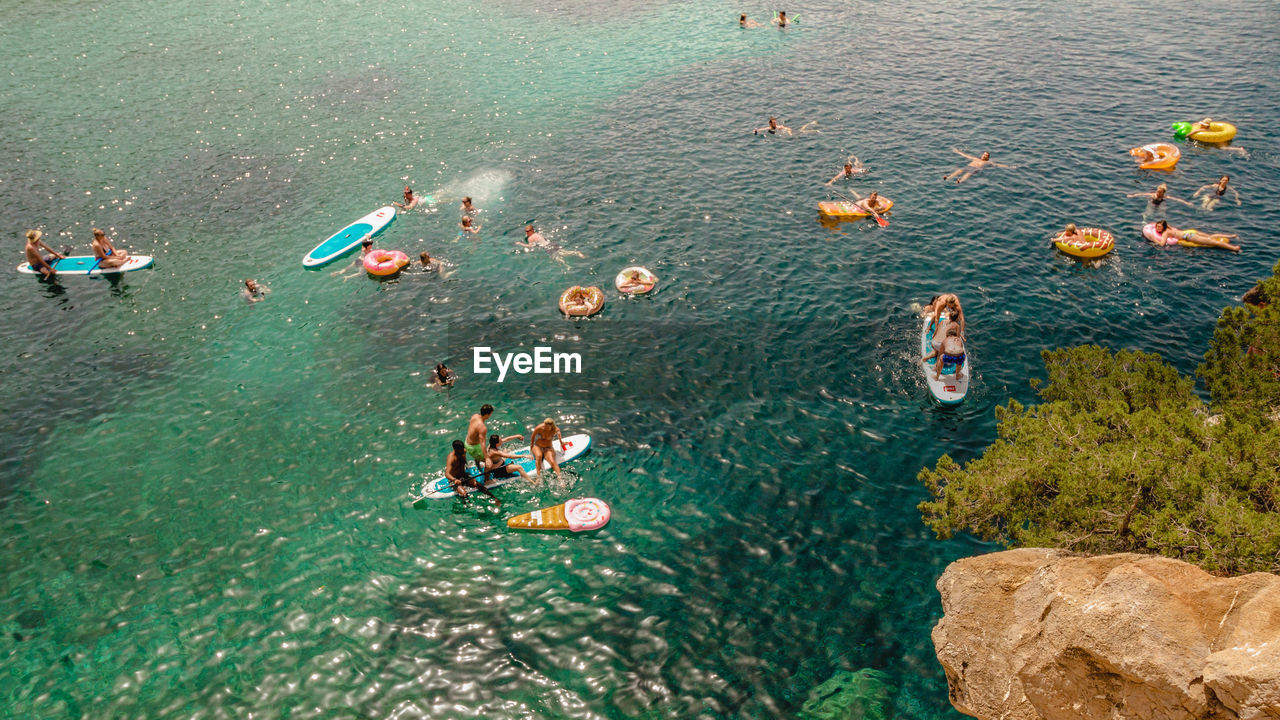 HIGH ANGLE VIEW OF PEOPLE ON ROCK IN SEA