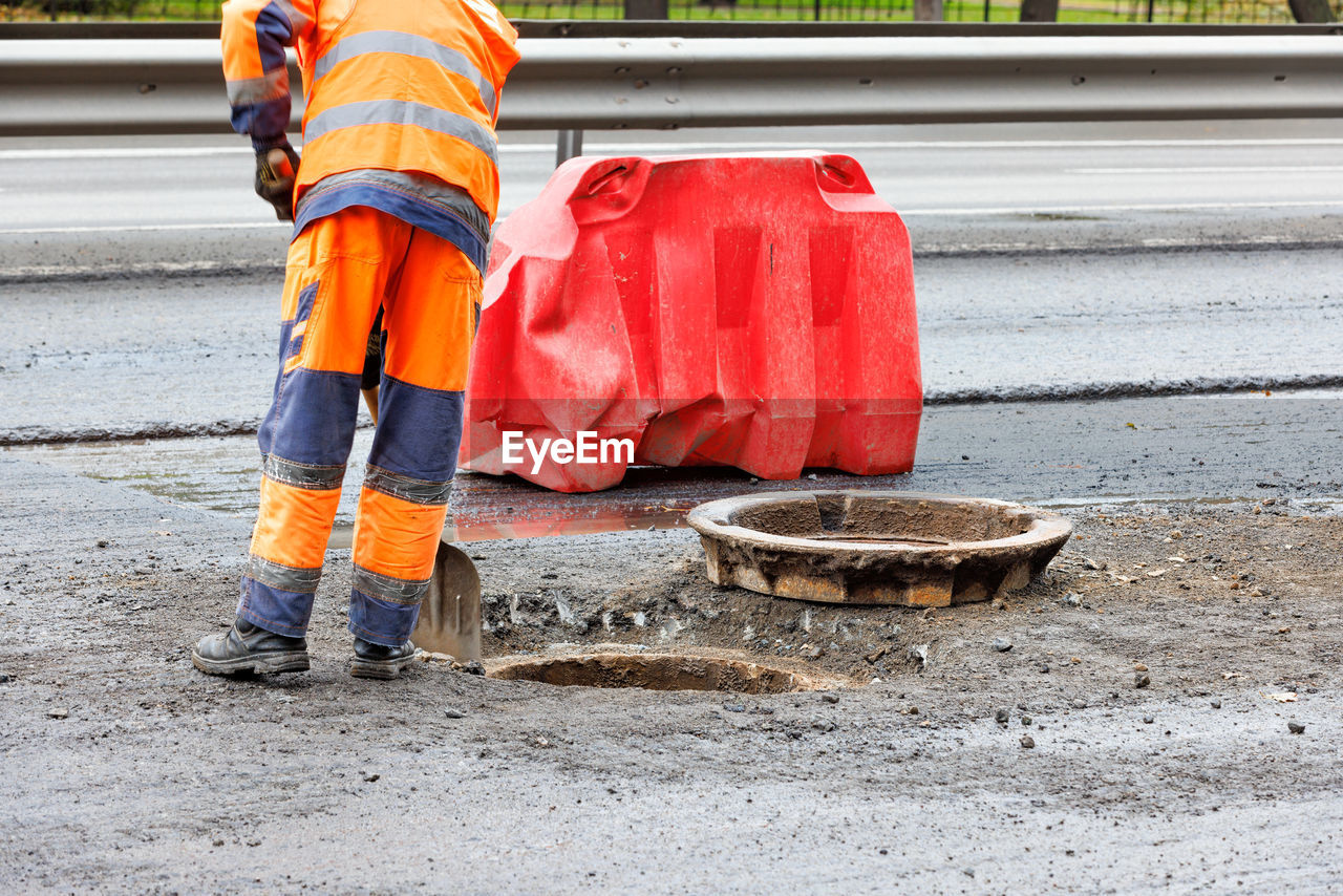 A road worker cleans the mouth of a sewer manhole on the carriageway.