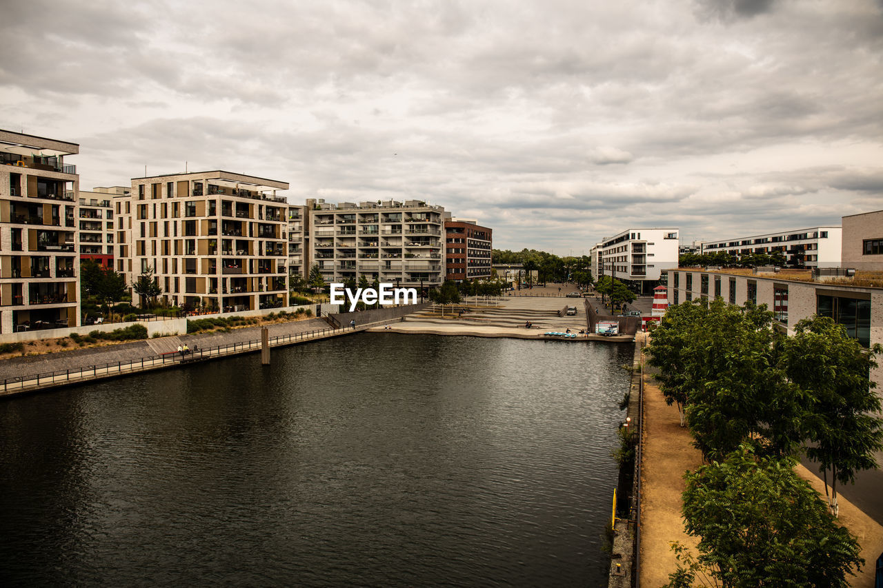 Buildings by river against sky in city