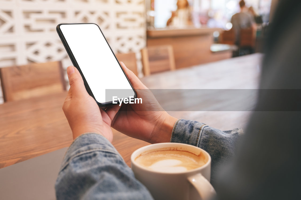 CROPPED IMAGE OF HAND HOLDING COFFEE CUP AND LAPTOP