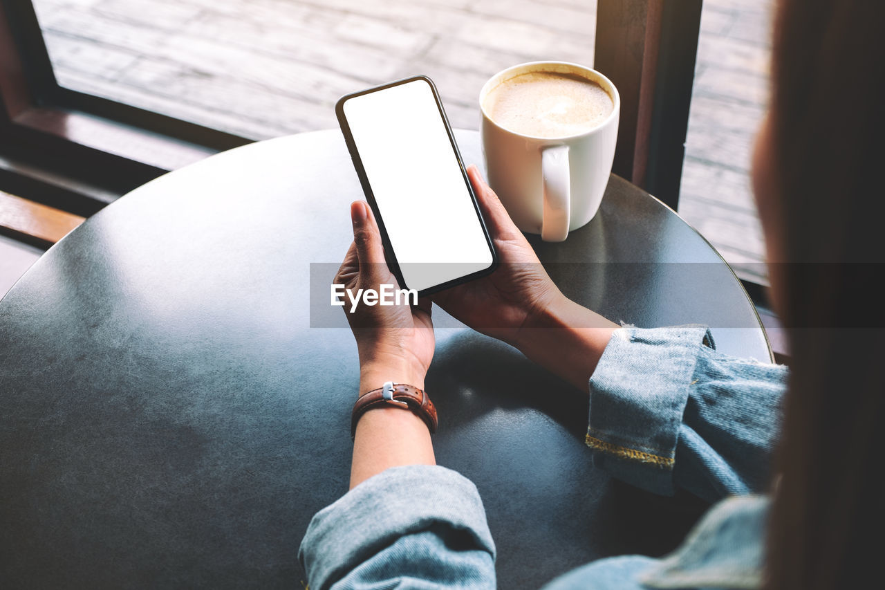 Cropped image of woman using blank phone at table in cafe