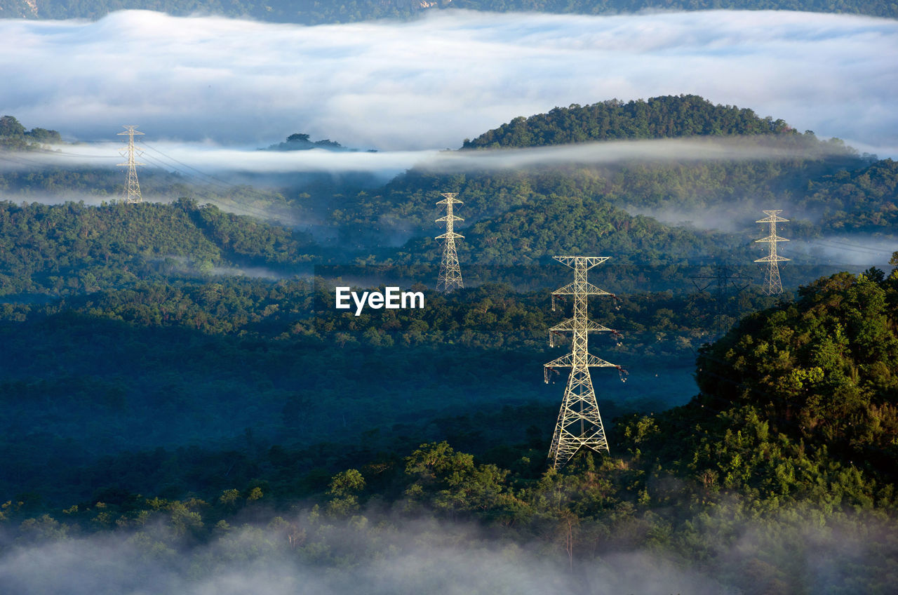 Transmission tower in green forest and beautiful morning smooth fog. high voltage power poles.