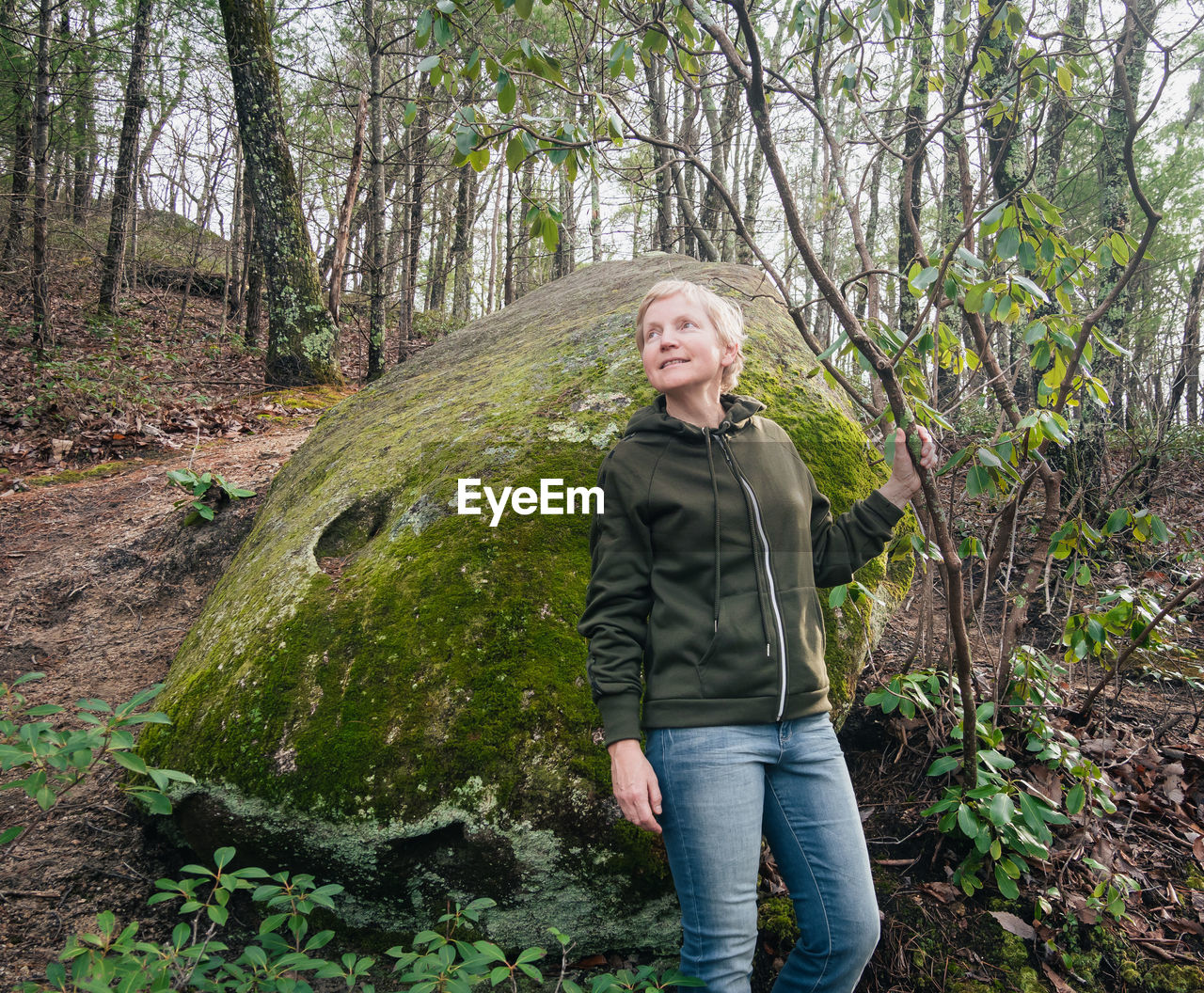 Woman looking away while standing by rock in forest