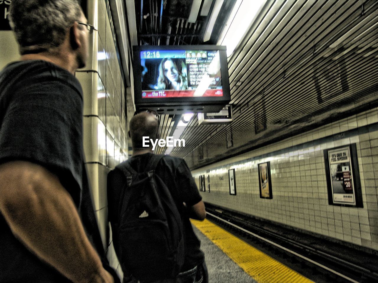 Rear view of people looking at monitor while waiting at subway station