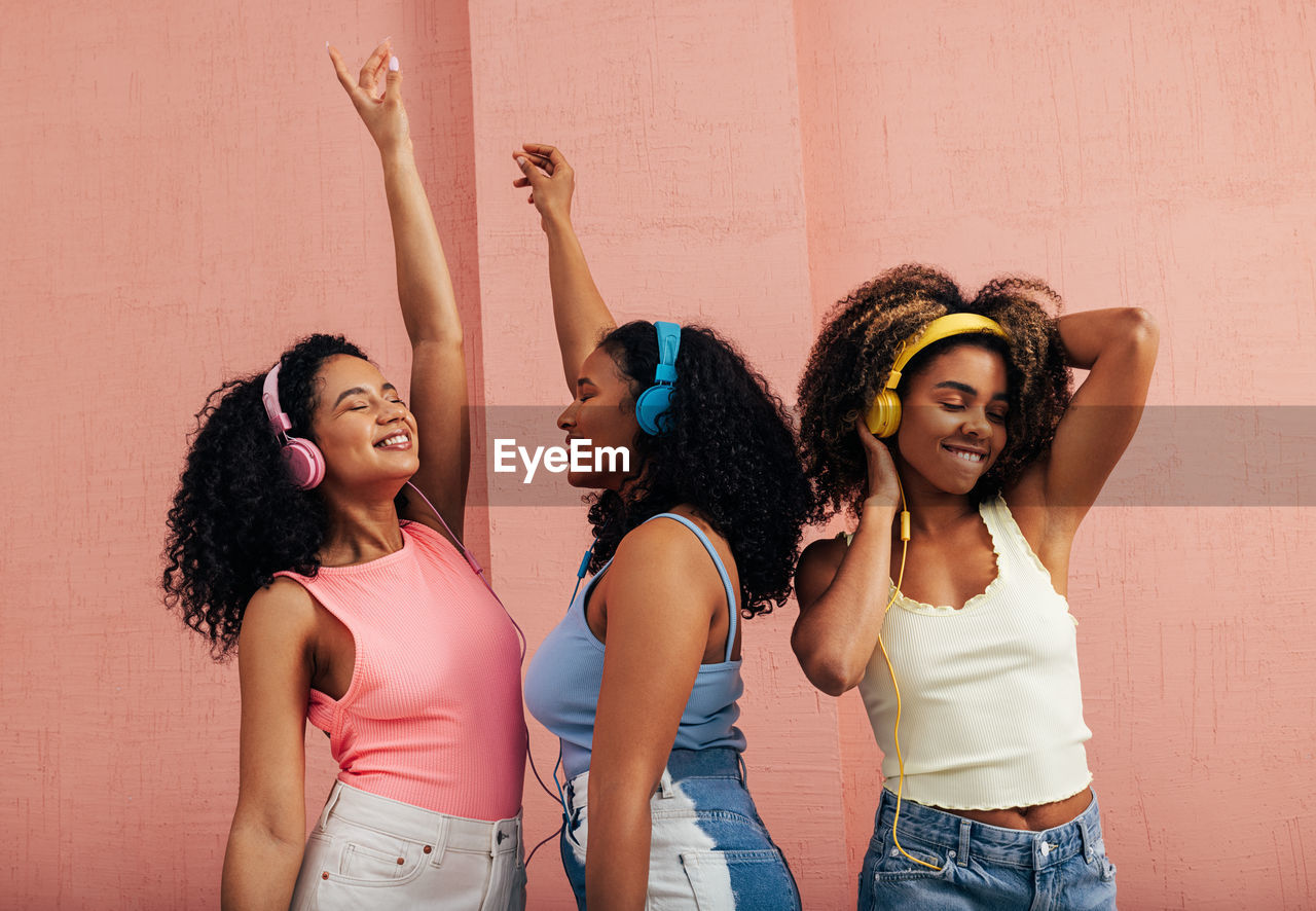 Female friends enjoying music against wall