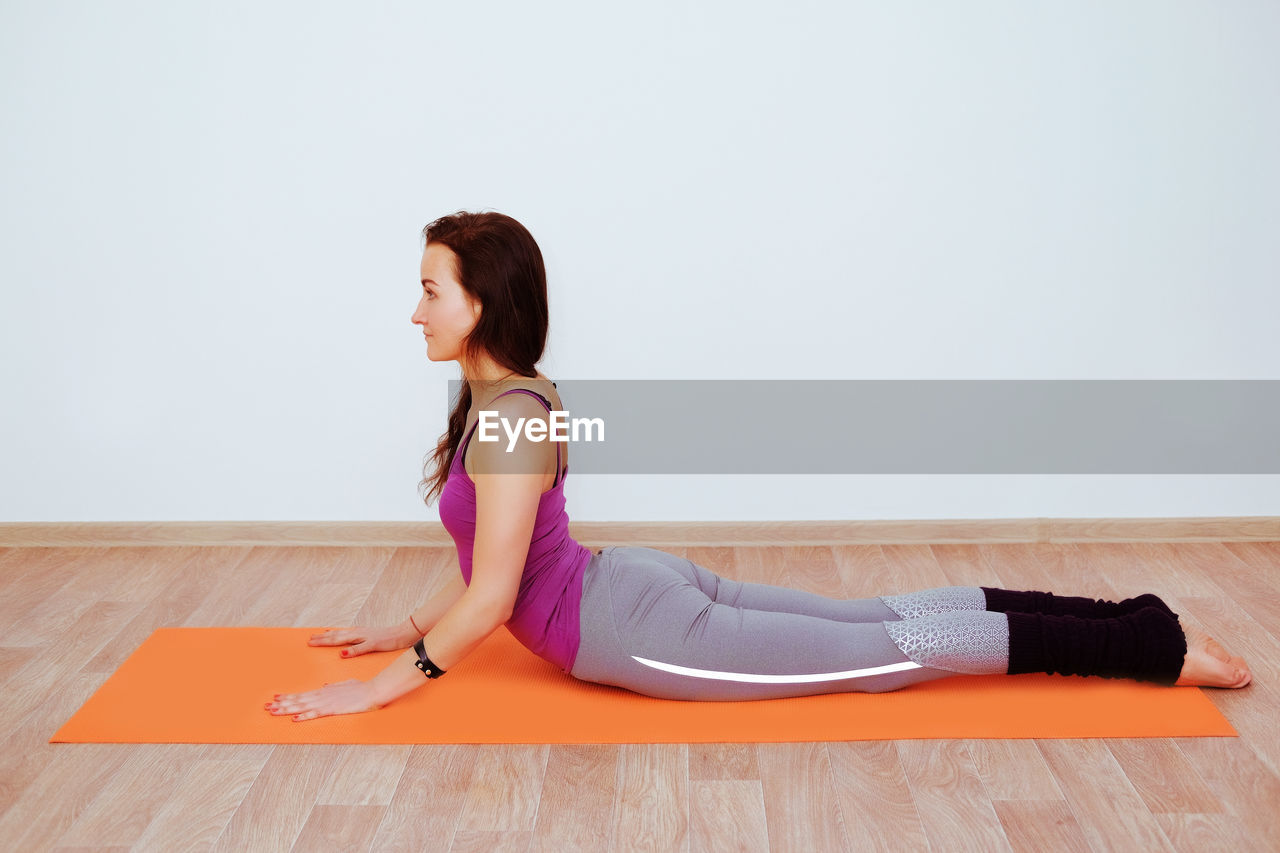 SIDE VIEW OF WOMAN SITTING ON HARDWOOD FLOOR AGAINST WALL