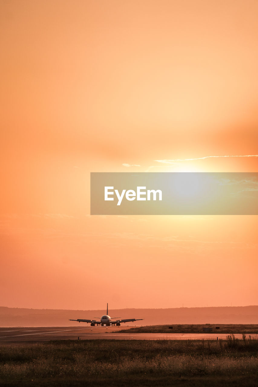 Airplane on runway against sky during sunset