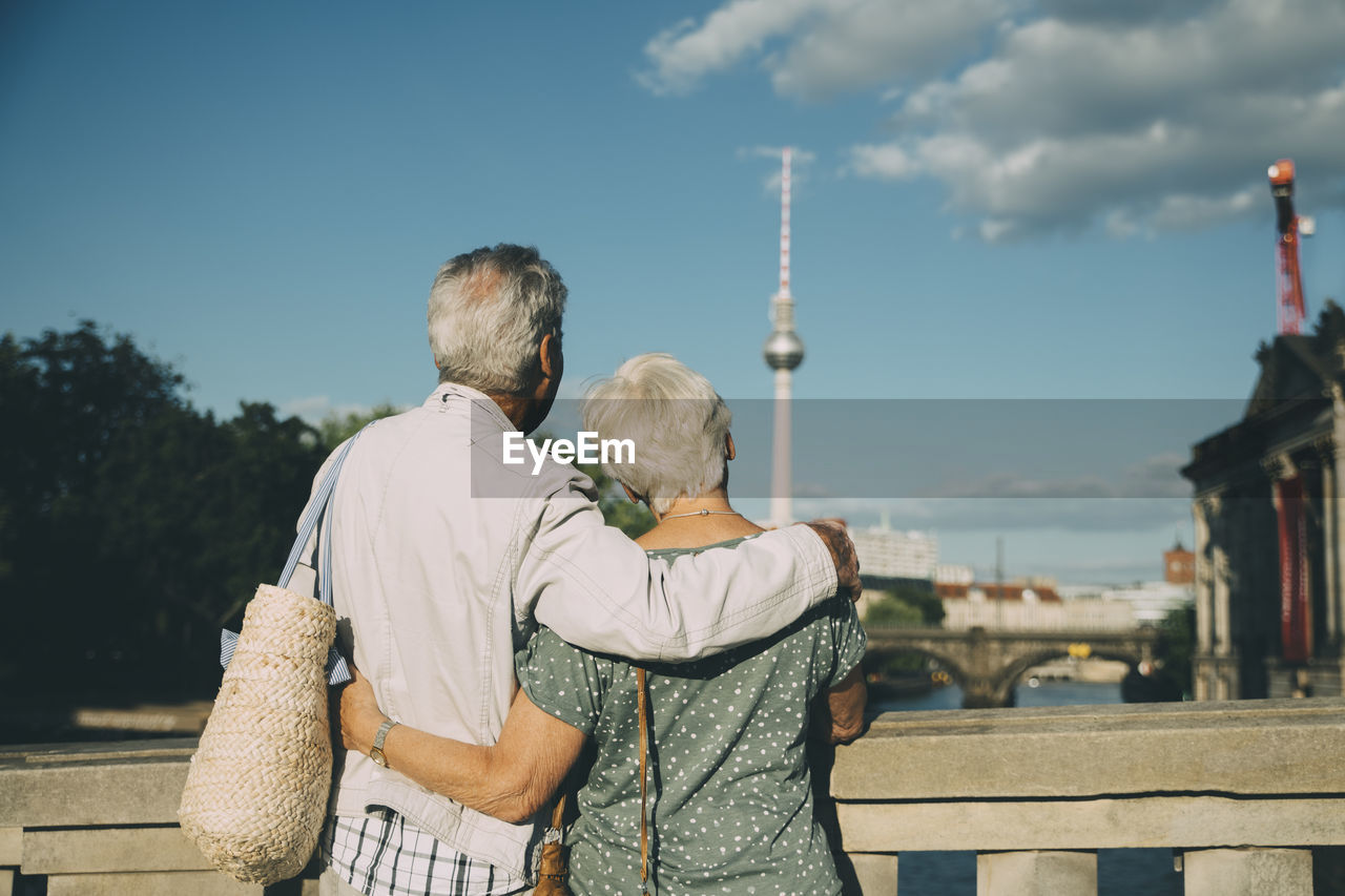 Rear view of senior couple with arm around looking at television tower from bridge in city