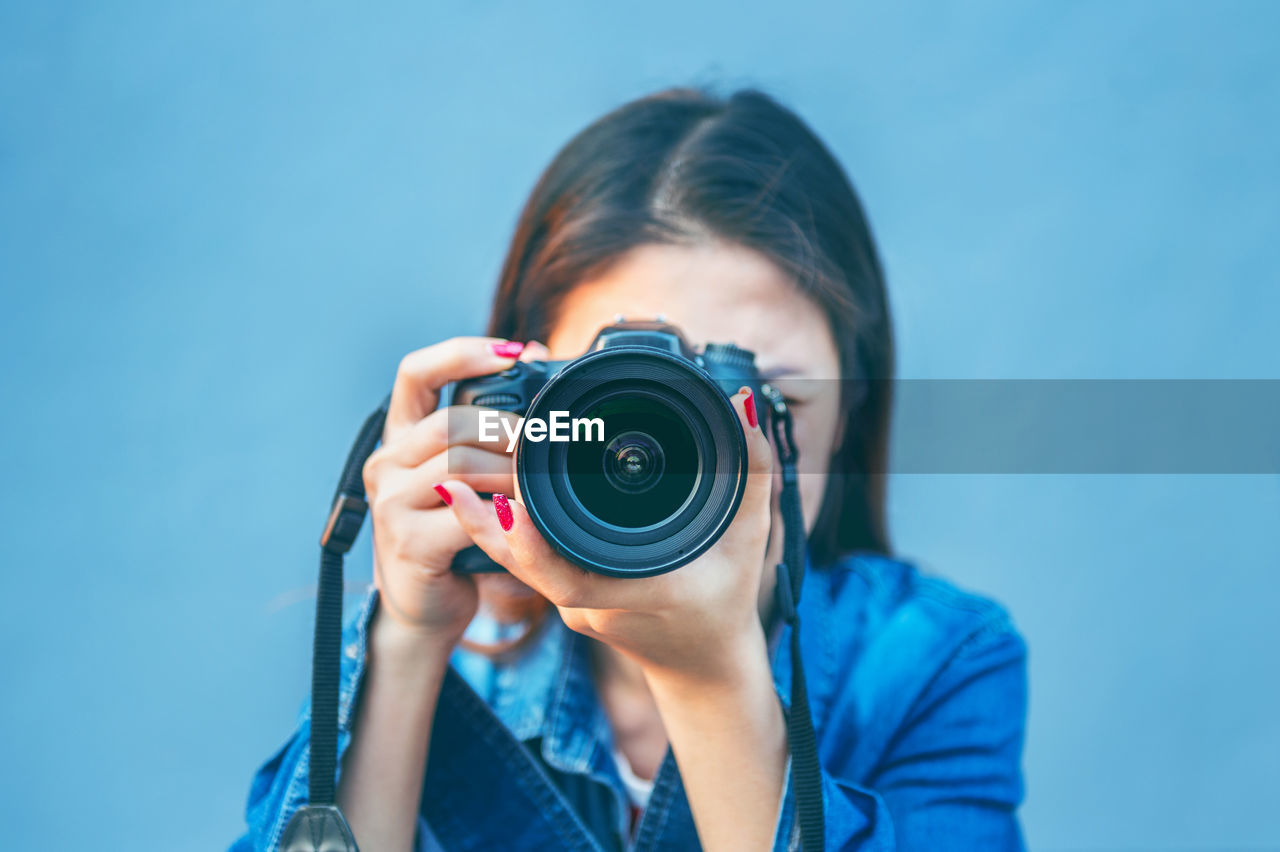 Woman photographing through camera against blue background