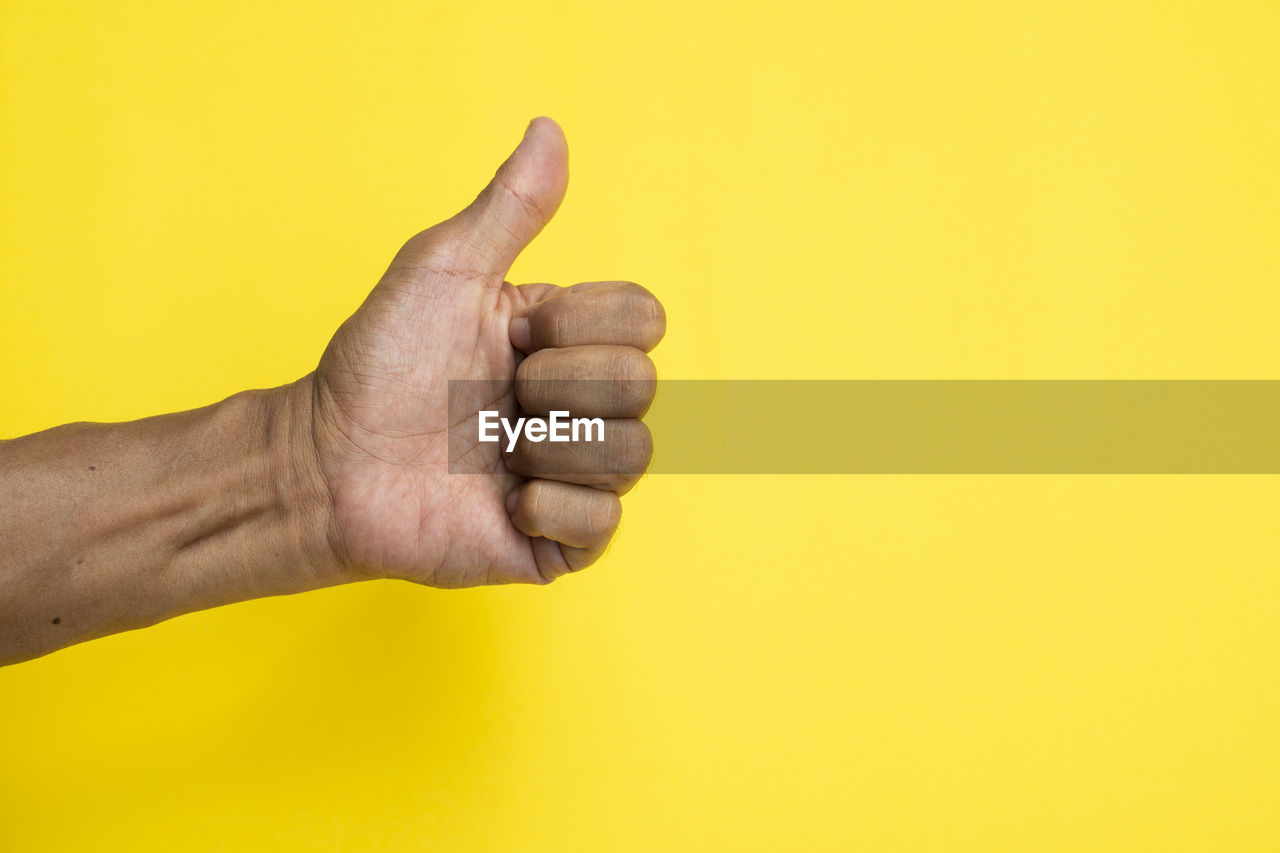 CLOSE-UP OF HUMAN HAND ON YELLOW BACKGROUND