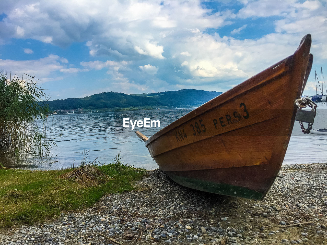 BOAT MOORED ON BEACH BY MOUNTAIN AGAINST SKY