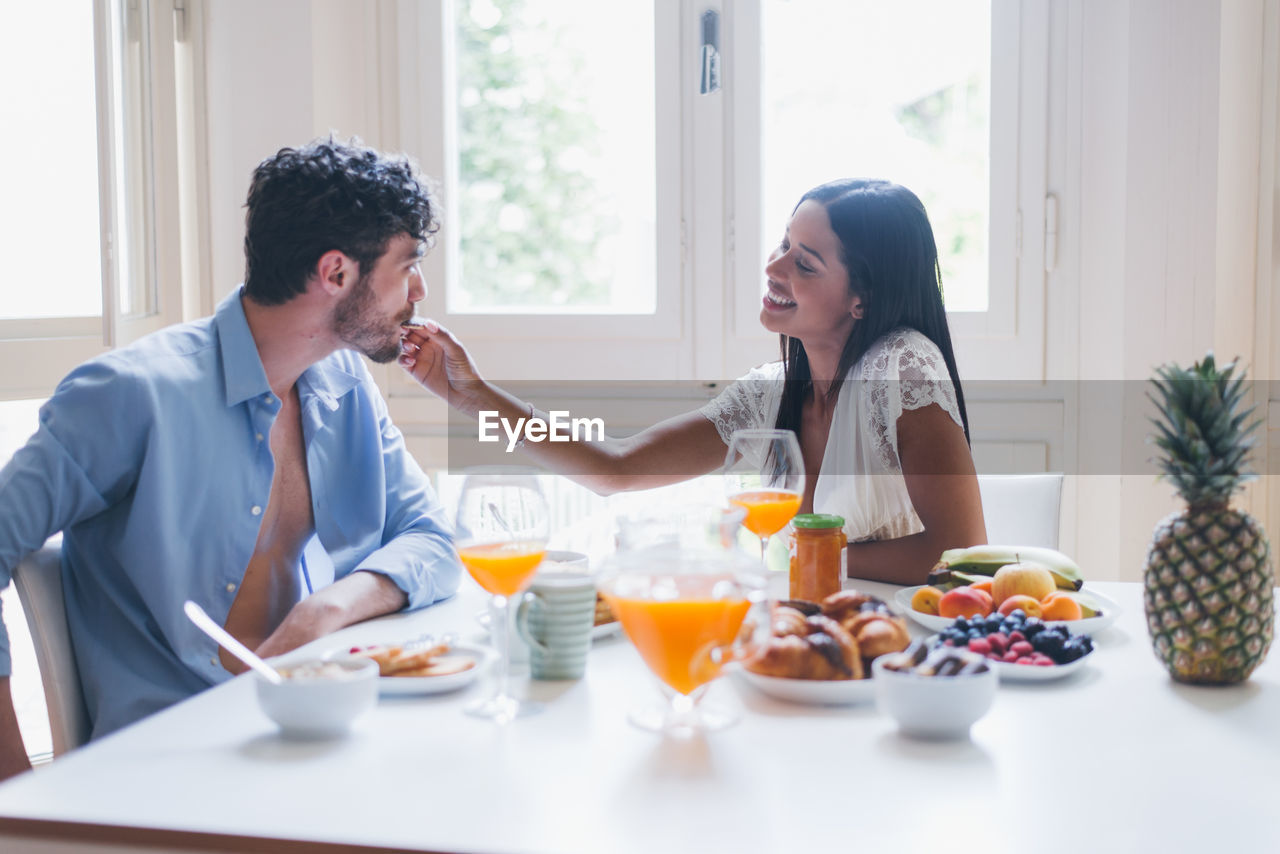 Smiling woman feeding breakfast to boyfriend at home